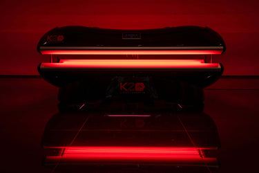 K2 red light therapy pod with glowing red lights in a dark room for full-body recovery and performance.